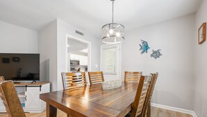 A dining area with a wooden table and chairs, a hanging light fixture, and decorative wall art. - Beach Square – optional BIKES – Walk 2 Redfern Village, shops, and restaurants!. (St Simons Island)