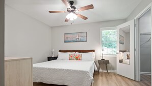 A bedroom with a bed, a ceiling fan, a window with blinds, and a painting on the wall. - Beach Square – optional BIKES – Walk 2 Redfern Village, shops, and restaurants!. (St Simons Island)