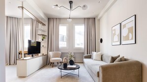 A modern living room with a flat-screen TV, a round coffee table, a beige sofa, and a white armchair. - Luxury Apartment in Plaka C (Athens)