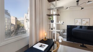 A modern hotel room with a city view, a desk with a lamp, a TV, and a bookshelf. - Luxury Apartment in Plaka C (Athens)