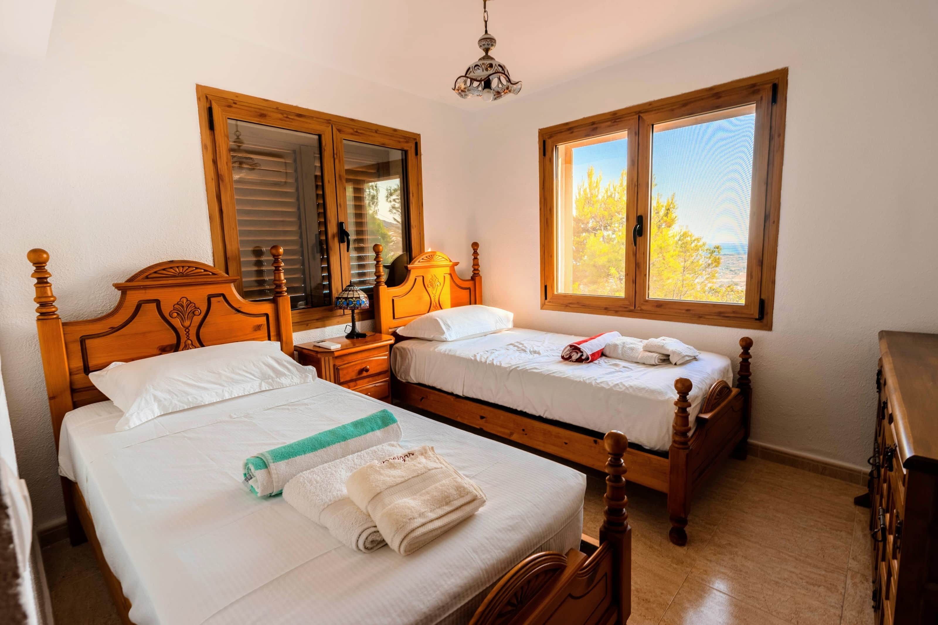 Une chambre à coucher avec deux lits en bois, une table de chevet, une commode et une fenêtre donnant sur des arbres.