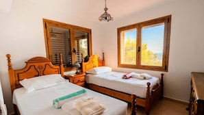 A bedroom with two wooden beds, a nightstand, a dresser, and a window with a view of trees. - Breizas Family House – Pool, Ocean Views & BBQ, Breizas House with Private Pool (Alcossebre)
