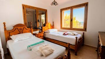 Une chambre à coucher avec deux lits en bois, une table de chevet, une commode et une fenêtre donnant sur des arbres.