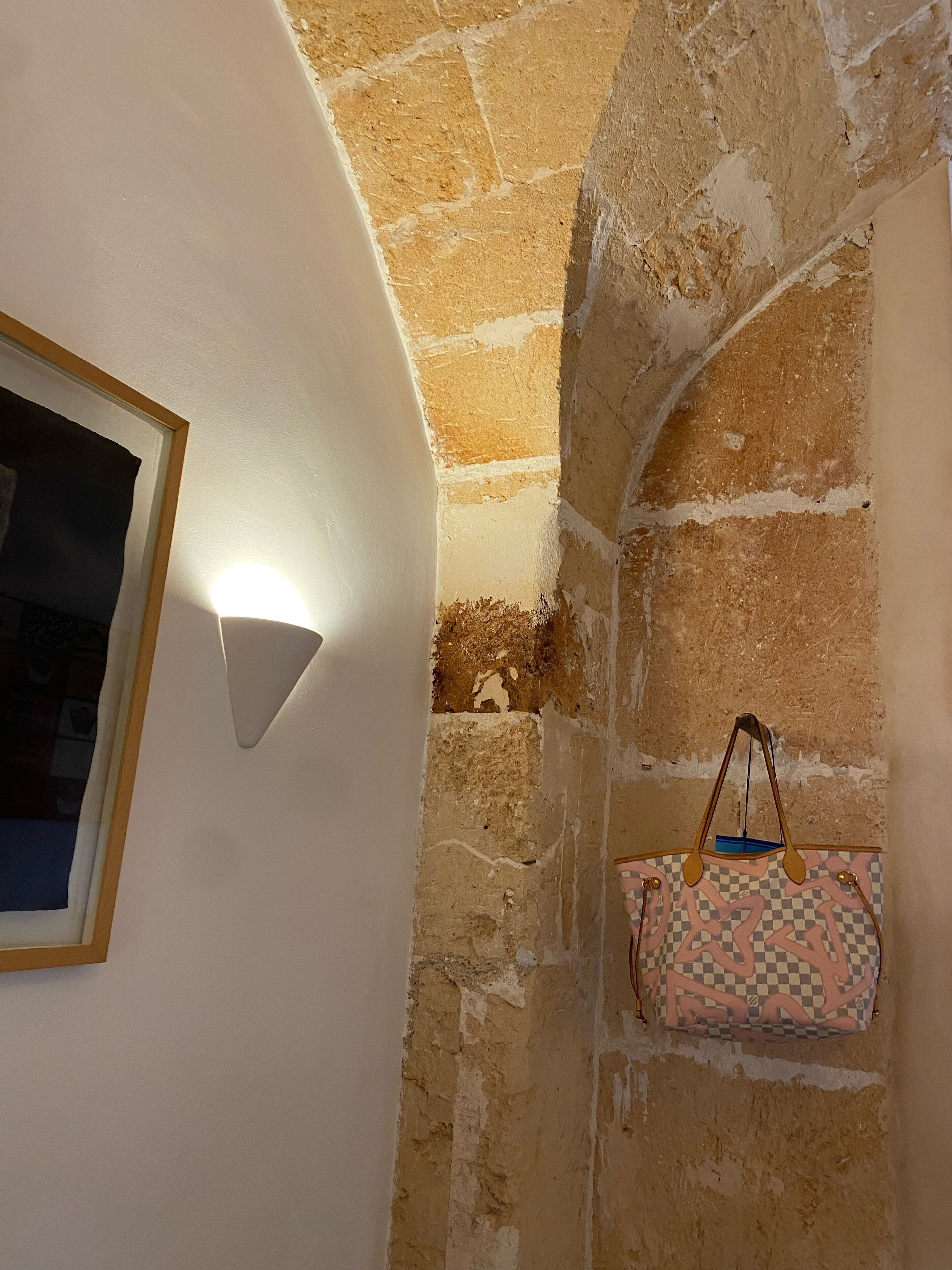 A room with a stone wall, a framed picture, and a hanging bag.