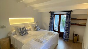 A modern bedroom with a large bed, a bedside table, a lamp, and a window with curtains. - Townhouse Cas Concos Santany (Cas Concos des Cavaller)