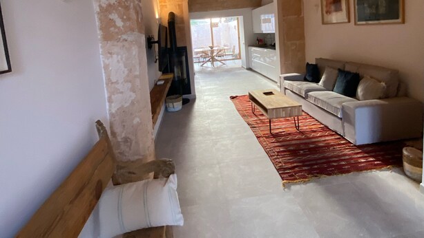 A spacious living area with a high ceiling, exposed brick walls, a wooden bench, a sofa, and a red rug. - Townhouse Cas Concos Santany (Cas Concos des Cavaller)