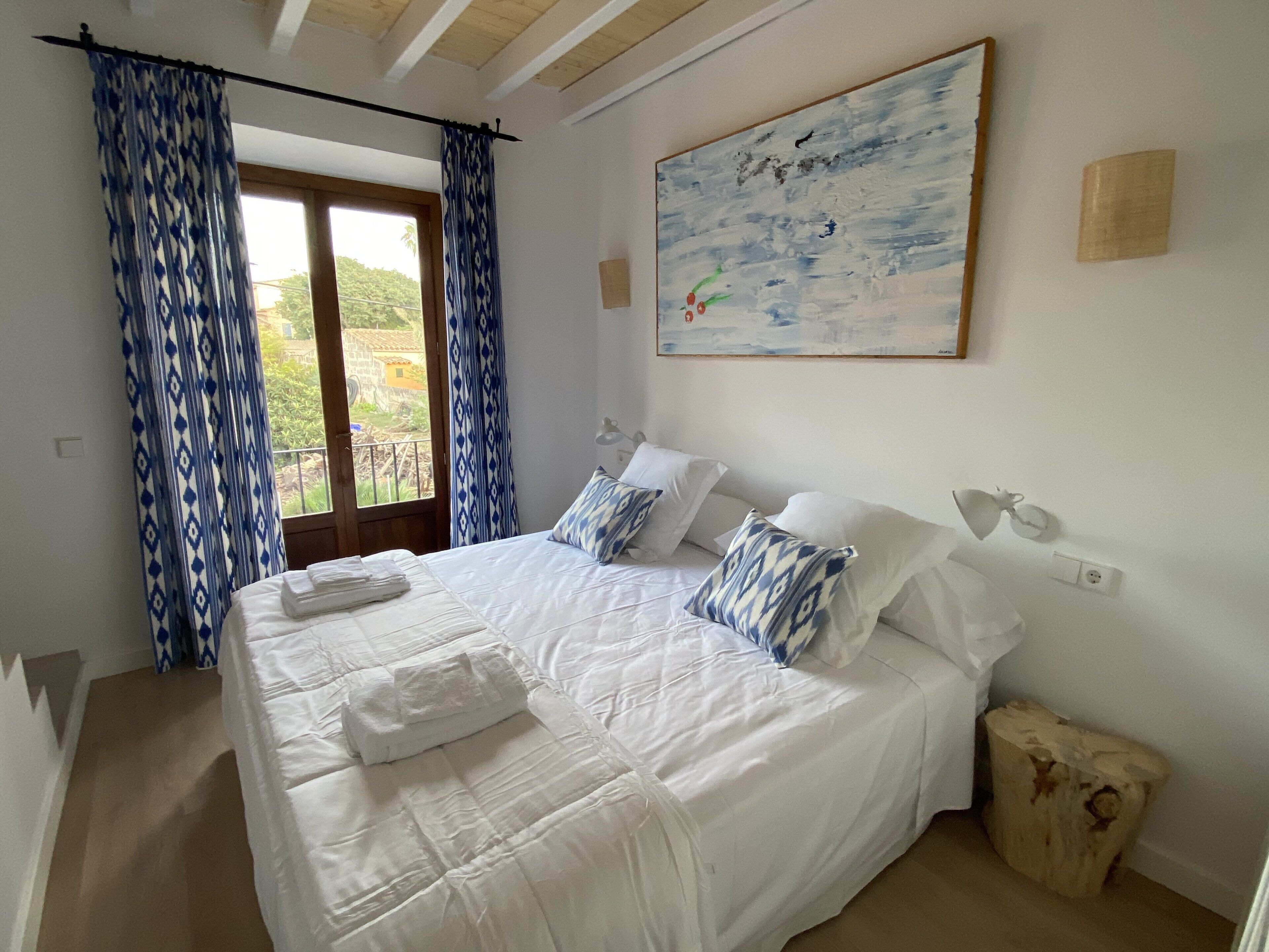 Un dormitorio con una cama grande, ropa de cama blanca y un cuadro en la pared.
