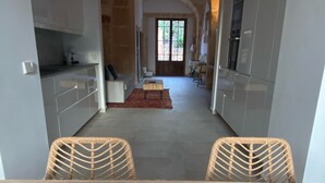 A modern kitchen with white cabinets, a dining area with wicker chairs, and a view of the living room through an archway. - Townhouse Cas Concos Santany (Cas Concos des Cavaller)