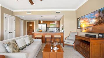 A spacious living area with a sofa, a coffee table, a TV, and a kitchen in the background.