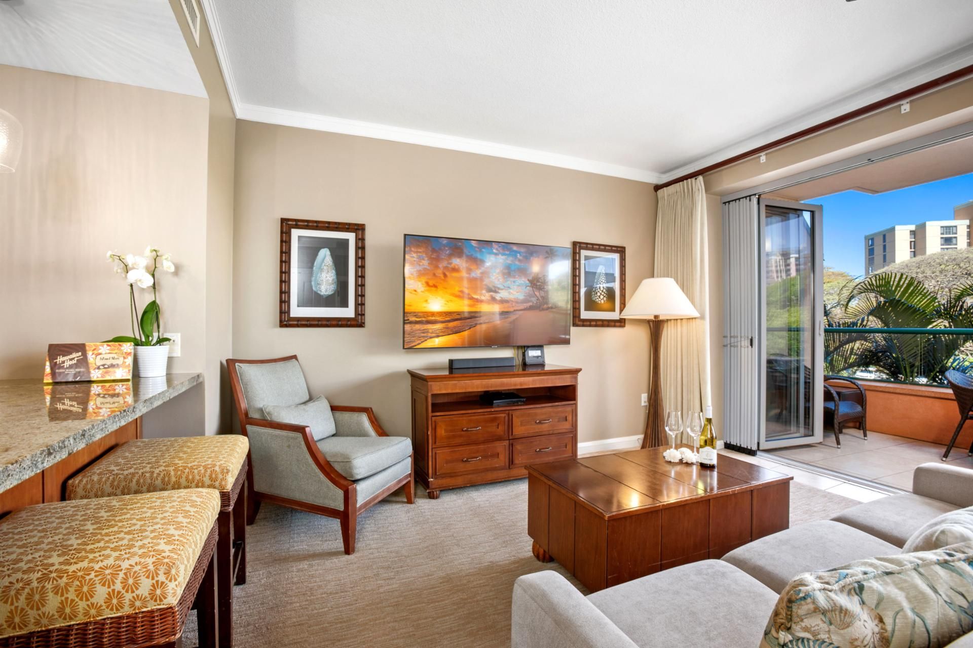 A hotel room with a large window, a flat-screen TV, a wooden coffee table, a sofa, a chair, a small table with a lamp, and a potted plant.