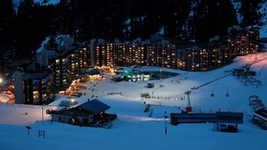 Estación de esquí nevada al anochecer, con edificios iluminados y un telesilla.