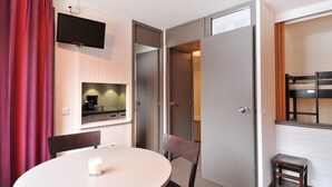 Una habitación compacta con una mesa de comedor, sillas, una pequeña cocina equipada con cafetera y un televisor montado en la pared.