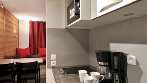 A compact kitchen with a stove, coffee maker, and white mugs on the counter. - travelski home select - Résidence Les Glaciers - Studio 3/4 personnes 318 (La Plagne)