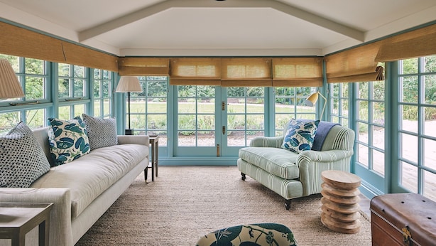 A conservatory with a high ceiling, large windows, and a cozy seating area with a sofa, armchair, and a small table. - Bridlepath Cottage - Luxury Cottages (Hungerford)