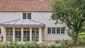 A two-story house with a tiled roof, a conservatory with multiple windows, and a garden with various plants. - Bridlepath Cottage - Luxury Cottages (Hungerford)