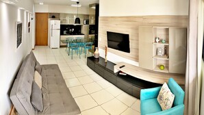 A modern living room with a grey sofa, a blue armchair, a flat-screen TV, and a kitchen in the background.