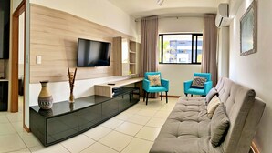 A modern living room with a flat-screen TV, a sofa, two armchairs, a coffee table, and a decorative vase.