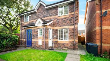 A two-story brick house with a blue front door, a visible number '55' on the wall, and a small front yard.
