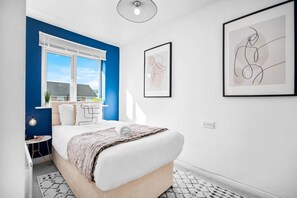 A bedroom with a bed, a window, a wall-mounted light fixture, and two framed artworks.