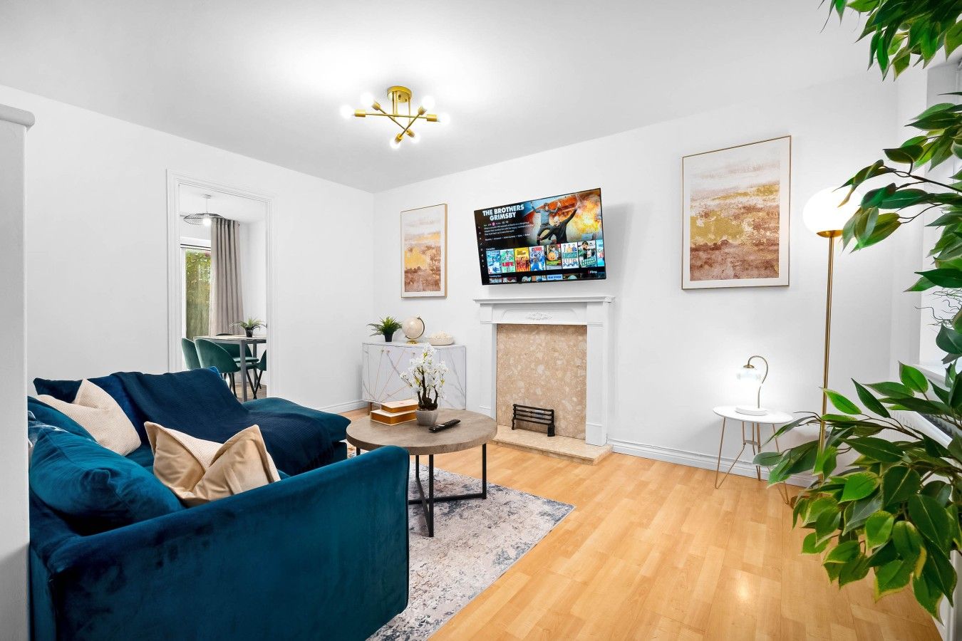 A living room with a blue sofa, a fireplace, a television mounted on the wall, and a large plant.