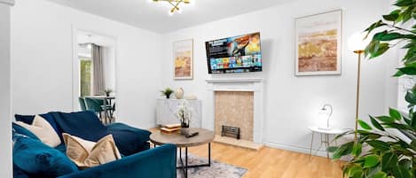 A living room with a blue sofa, a fireplace, a television mounted on the wall, and a large plant.