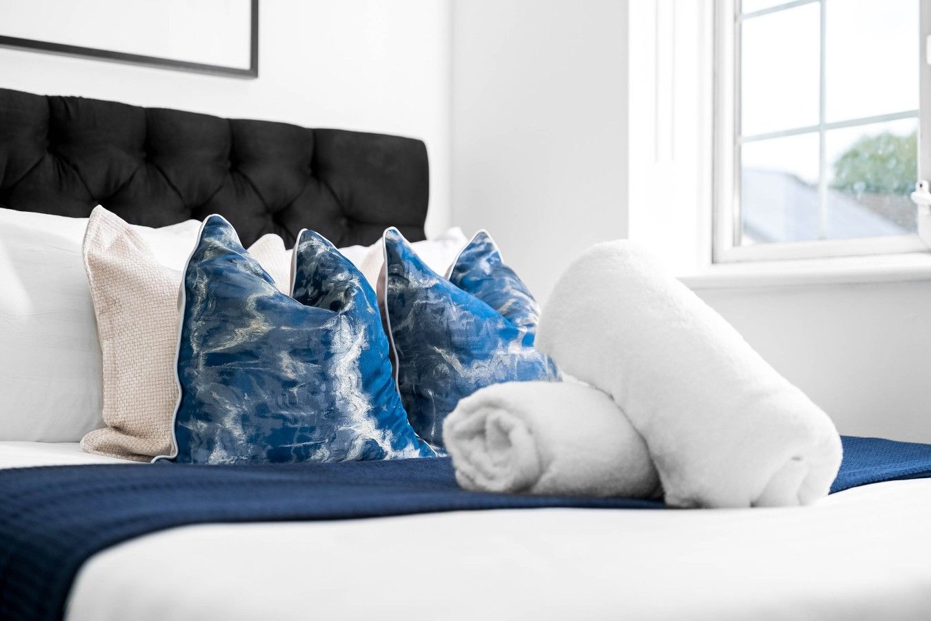 A bed with a black headboard, white bedding, and blue and white pillows.