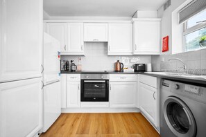 A modern kitchen with white cabinets, a built-in oven, a washing machine, and a window with a view.