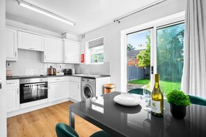 Una cocina moderna con armarios blancos, horno empotrado, lavadora y comedor con mesa y sillas.