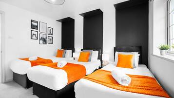 A hotel room with three beds, black and white bedding, orange accents, and a large window.