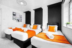 A hotel room with three beds, black and white bedding, orange accents, and a large window.