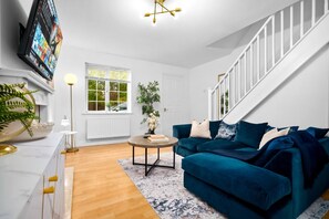A living room with a blue sofa, a round coffee table, a white fireplace, and a TV mounted on the wall. - Stylish Two Bed House - Garden - Parking - WIFI (West Midlands)