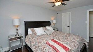 Une chambre à coucher avec un lit, deux tables de chevet, un ventilateur de plafond et une porte.