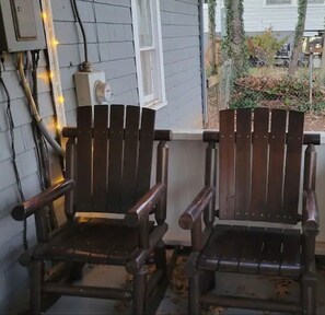 Zwei hölzerne Adirondack-Stühle auf einer Veranda mit weißem Geländer, einer Steckdose und einer Lichterkette.