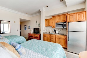Une chambre avec deux lits, une kitchenette dotée de meubles en bois, un four à micro-ondes et un réfrigérateur.