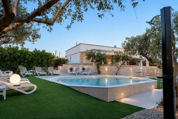 A modern outdoor pool area with lounge chairs, a hot tub, and a stone wall.