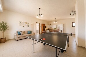 A living room with a ping pong table, a sofa, a dining table, and a kitchen in the background.