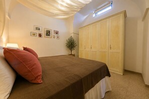 Un dormitorio con cama, armario, una pequeña planta en maceta y cuadros colgados en la pared.
