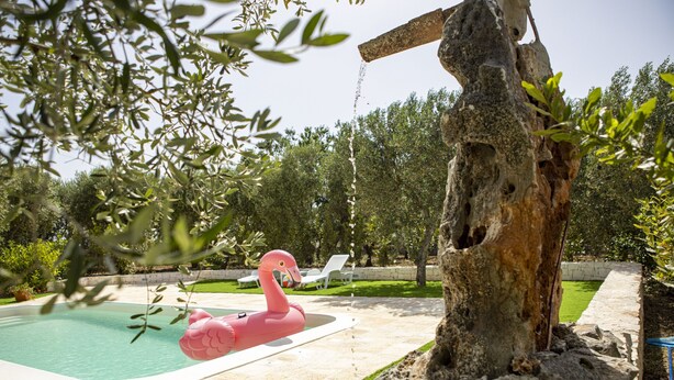 A swimming pool with a flamingo float, surrounded by a stone wall and trees. - ancient villa converted into a luxury residence by pugliadamare (Martina Franca)
