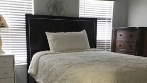 Un dormitorio con un cabecero negro, ropa de cama blanca, una alfombra blanca y una mesita de noche de madera.