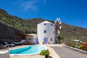 A white building with a pool, surrounded by stone walls and a windmill.