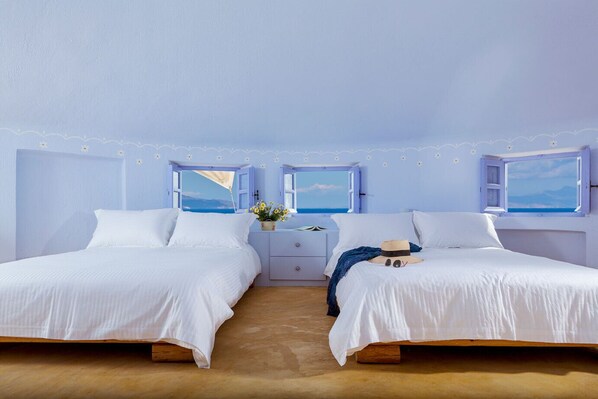 A twin bedroom with two beds, a nightstand, and a window with a view of the sea.