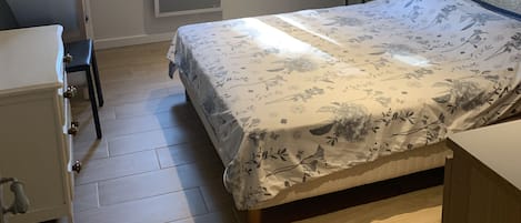 A bedroom with a bed, a dresser, a window, and a radiator.