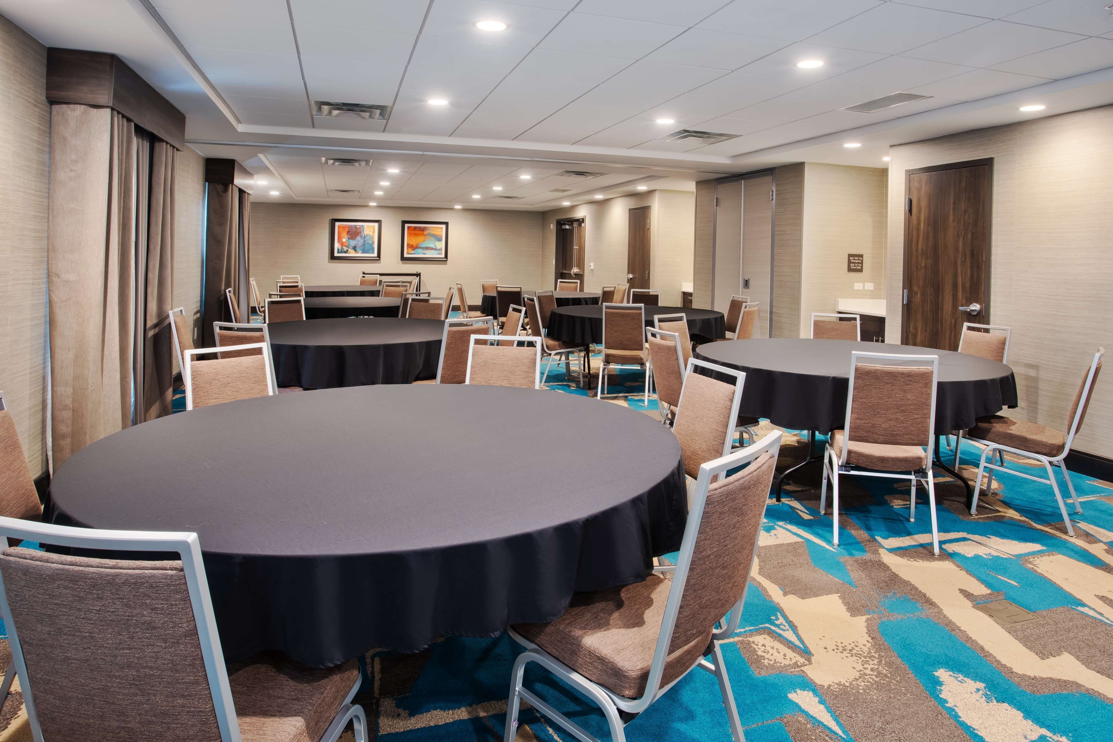 A conference room with round tables and chairs, a carpeted floor, and a door in the background.