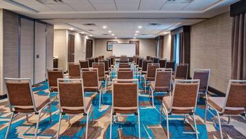 A conference room with rows of chairs, a projector screen, and a carpeted floor.
