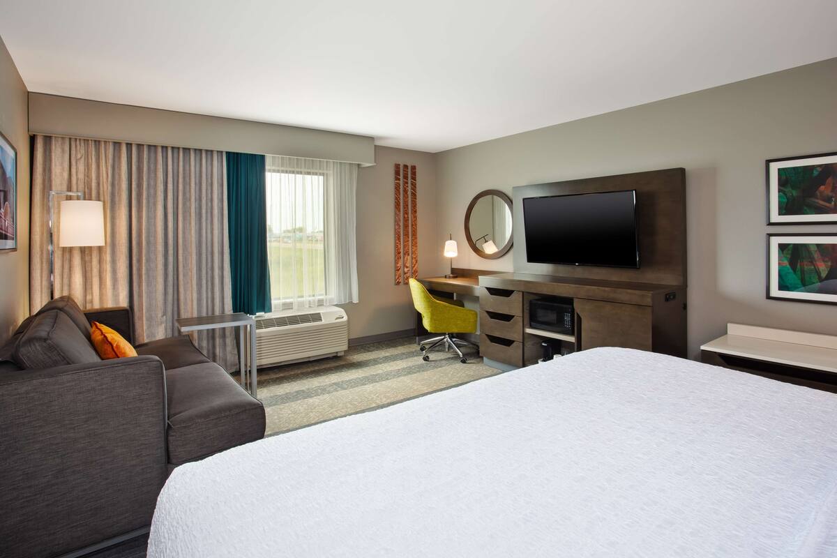 A hotel room with a bed, a desk, a chair, a TV, and a window with curtains.