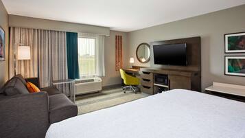 A hotel room with a bed, a desk, a chair, a TV, and a window with curtains.