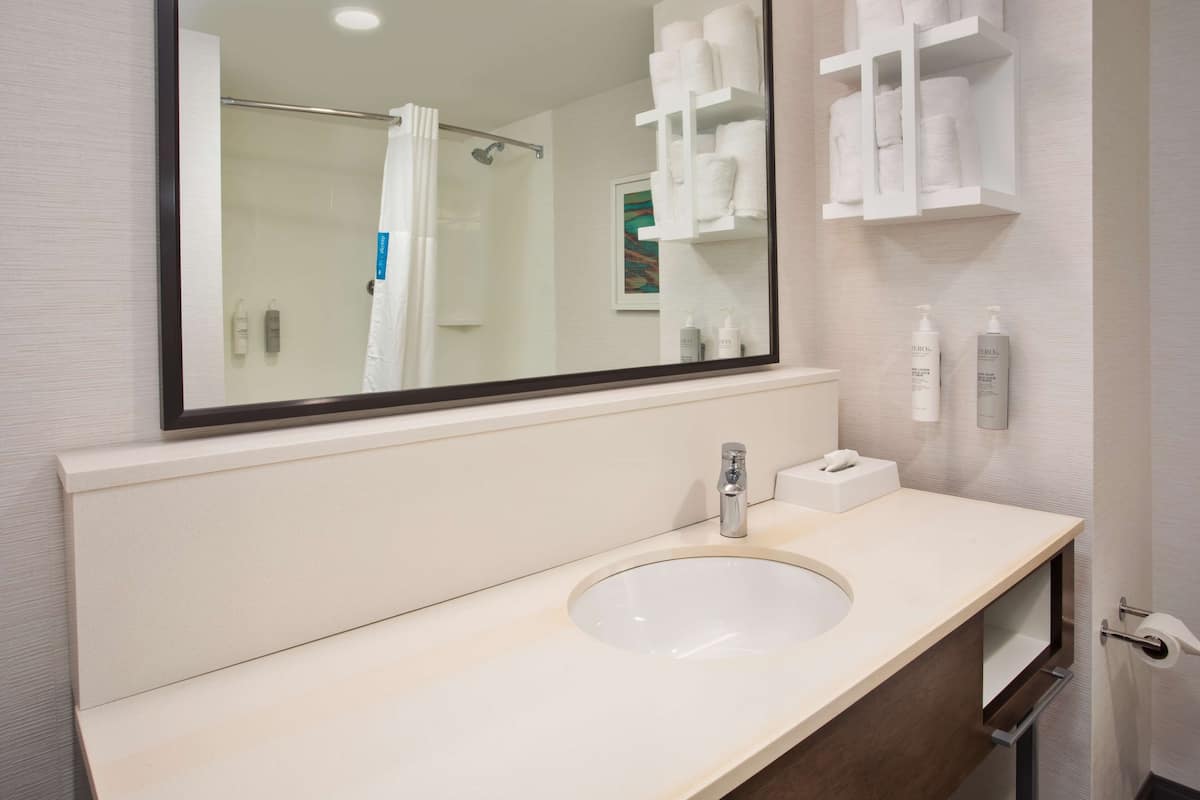 A modern bathroom with a large mirror, a sink, and a shower area.