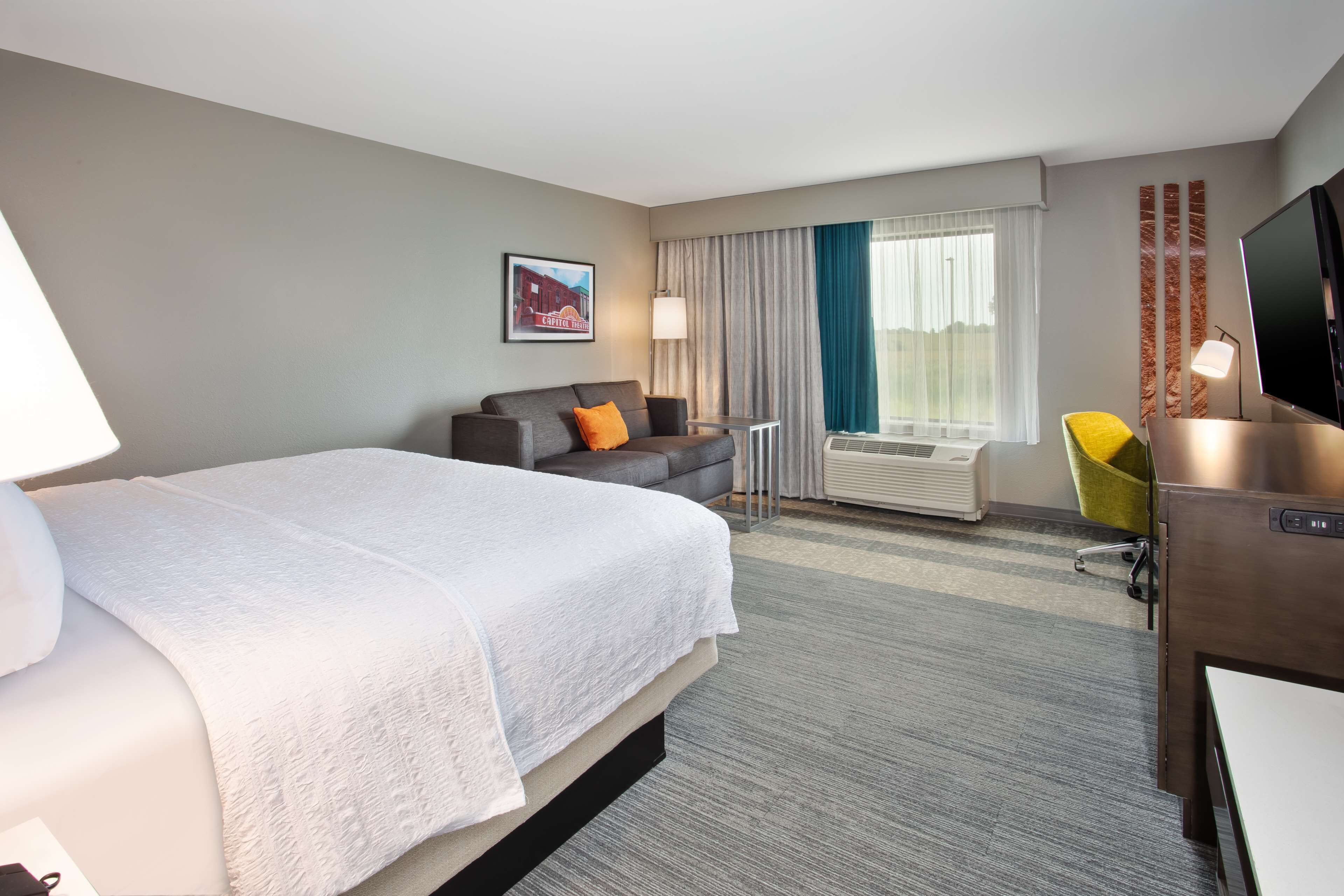 Une chambre d’hôtel avec un grand lit, un canapé, un bureau avec une télévision et une fenêtre avec des rideaux.