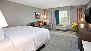 Une chambre d’hôtel avec un grand lit, un canapé, un bureau avec une télévision et une fenêtre avec des rideaux.