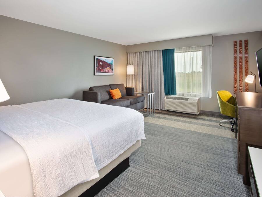 Une chambre d’hôtel avec un grand lit, un canapé, un bureau avec une télévision et une fenêtre avec des rideaux.